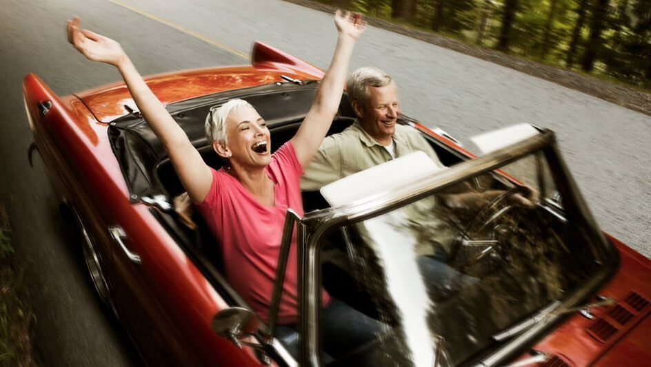 Mature couple riding in a convertable through a forest