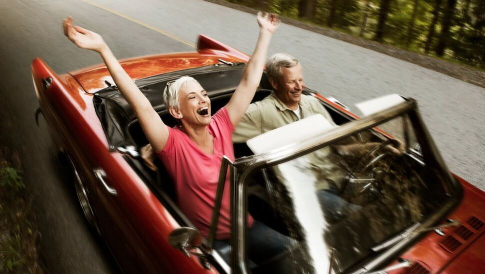 Mature couple riding in a convertable through a forest